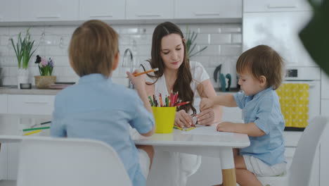Zwei-Kinder-Eines-Jungen-Zeichnen-Mit-Seiner-Mutter,-Die-In-Der-Küche-Sitzt.-Glückliche-Familie-Zu-Hause.